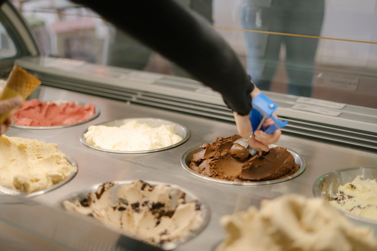 A hand scoops chocolate ice cream in a vibrant gelato shop in Perth, Australia. Indulge your sweet tooth.